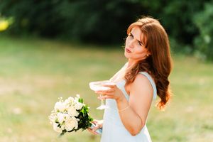 Bride in white dress twirls joyfully in outdoor garden setting with natural sunlight.