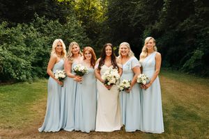 A group in coordinated powder blue and white dresses pose together in an outdoor garden setting.