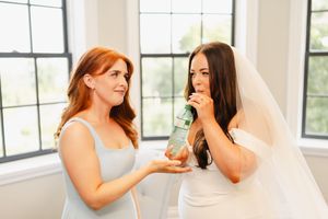Two women share an emotional moment while wearing wedding attire in a bright indoor setting.