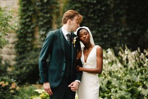 A romantic wedding couple shares intimate moments in a lush garden setting with ivy-covered walls.