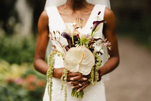 Elegant white bridal bouquet with lilies and greenery held against a white wedding dress.