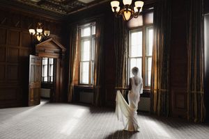 A sunlit hallway in an ornate historic building with wood-paneled walls and elegant chandeliers casting warm light.