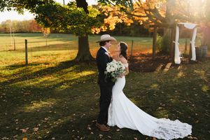 A romantic outdoor wedding photoshoot in a golden sunlit field with autumn trees and fallen leaves at sunset.