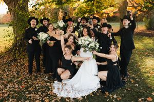 Wedding party members playfully toss leaves during an autumn outdoor photo session in golden sunlight.