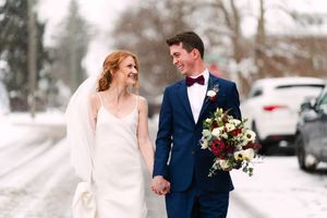 A couple shares a joyful moment in their wedding attire while walking through a snowy winter landscape.