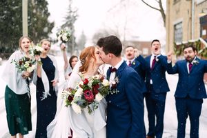 Wedding party in navy suits and white dresses pose together outdoors during winter celebration.
