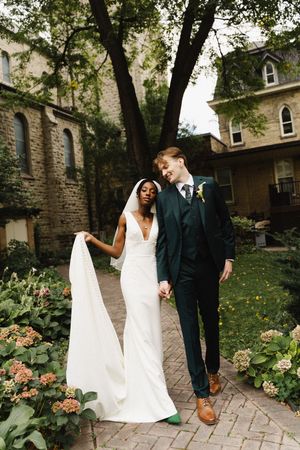 A couple shares a joyful moment together on a garden path surrounded by stone buildings and blooming flowers.