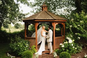 Wedding ceremony taking place in a wooden gazebo surrounded by gardens.