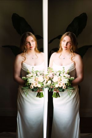 A dramatic wedding portrait series showing a person in white holding a lush bouquet of white flowers against dark shadows.
