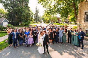 Wedding guests gather outdoors on a sunny day for group photos at a scenic venue.