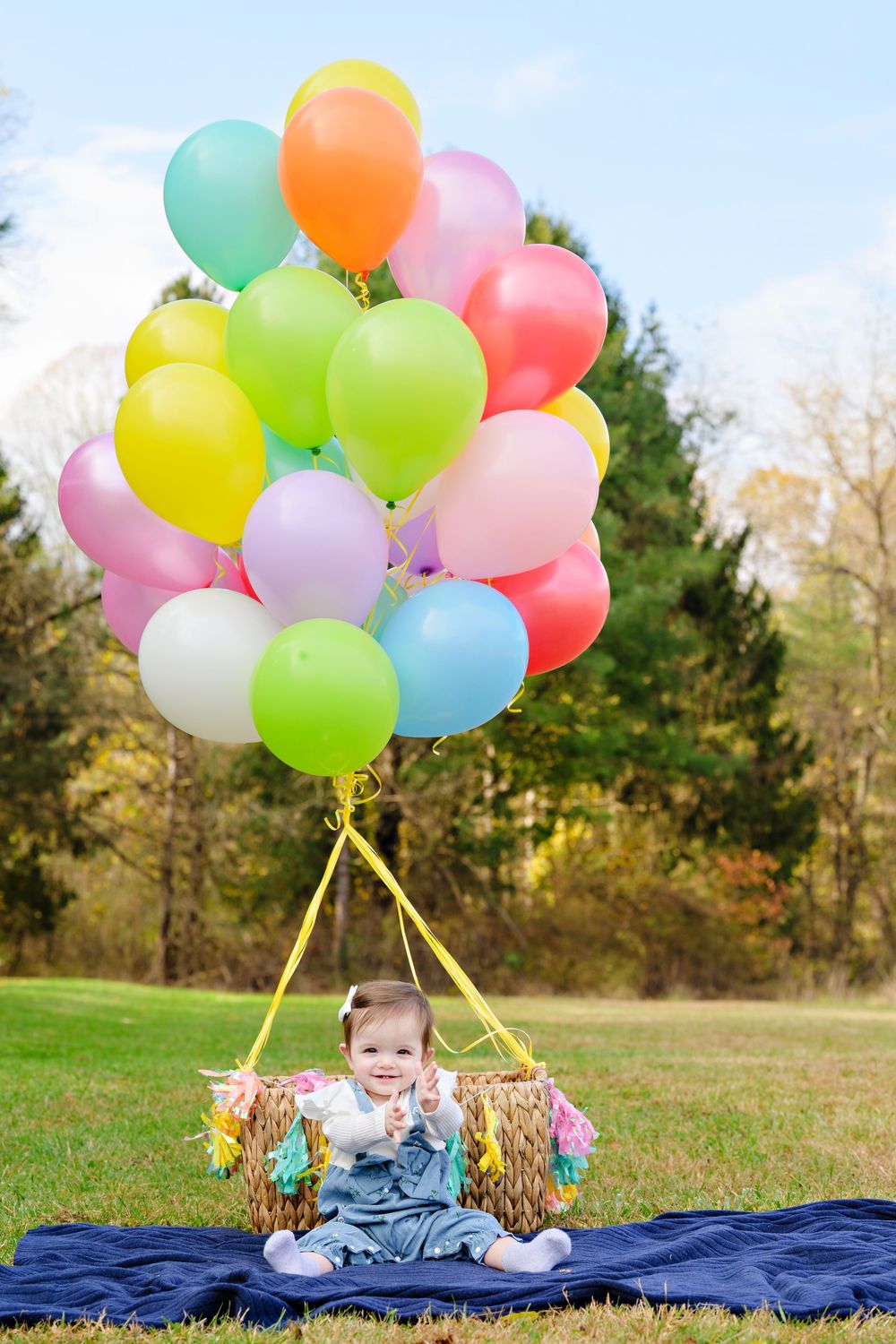 Colorful helium balloons tied together float above a blue blanket laid out on green grass at Brecksville Park portrait session