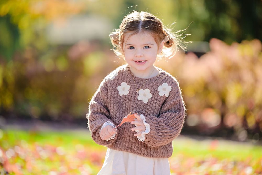 A child in a brown sweater plays outdoors on a sunny autumn day with golden leaves in the background at Gervasi Vineyard in Canton portrait