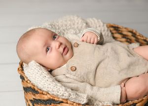 Baby wearing beige sweater resting in rustic woven basket.
