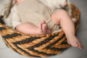 Close-up of tiny feet and legs in woven basket during newborn photoshoot.