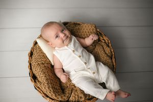 Infant in white outfit lying peacefully in brown woven basket.