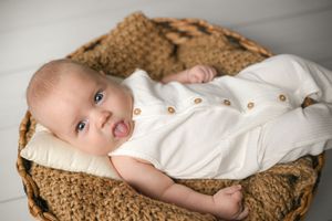 Baby in cream colored outfit resting in textured brown basket.