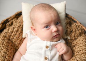 Close-up portrait of infant in white knit sweater on textured brown background.
