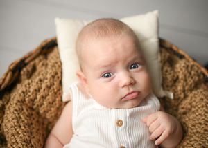 Baby wearing white turtleneck with wooden buttons on brown textured blanket.