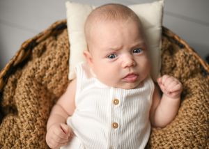 Infant in white sweater lying on brown textured backdrop during photo session.