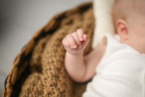 Side view of baby in white turtleneck against brown textured background.
