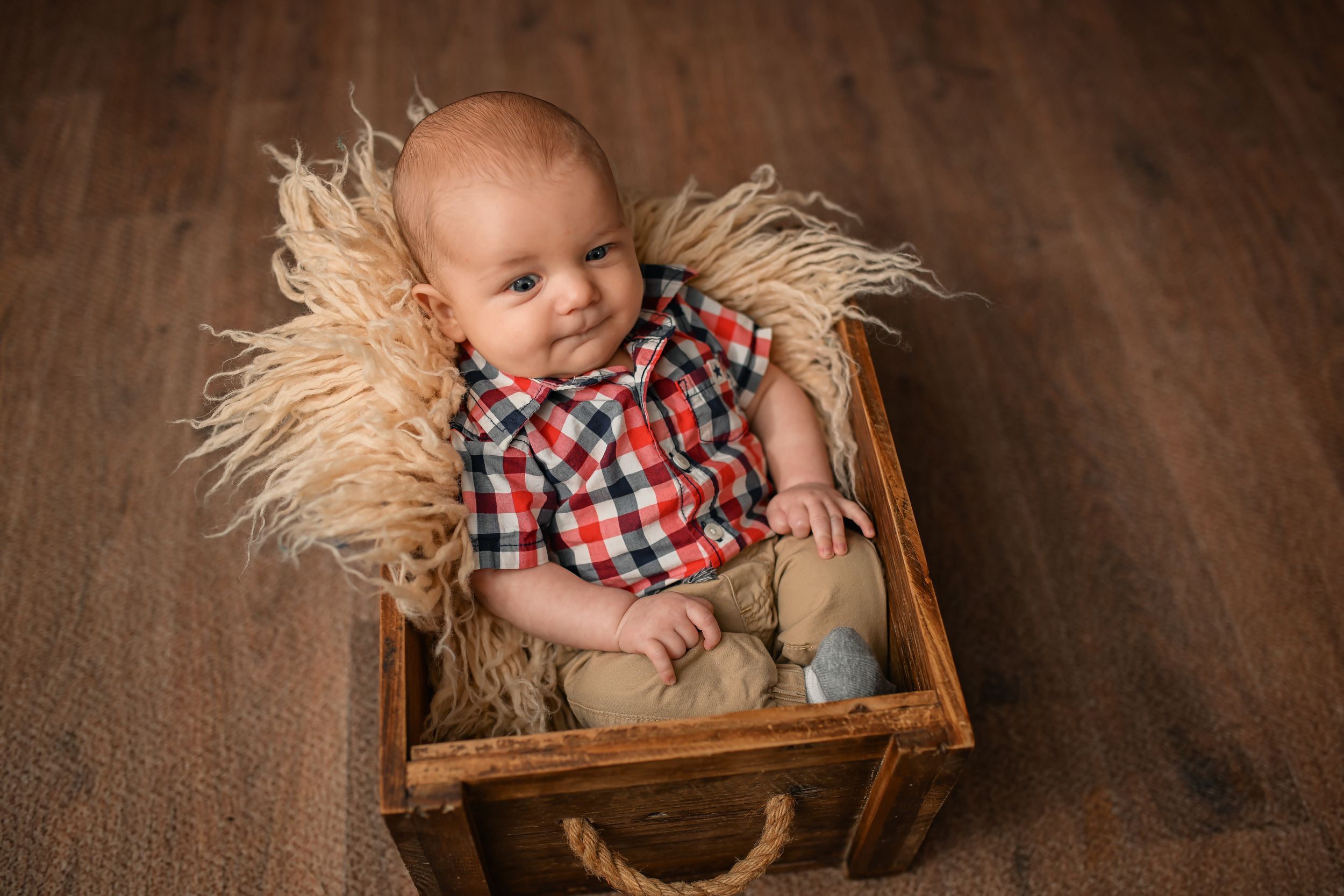 Baby resting in wooden box with straw bedding near warm fireplace glow.