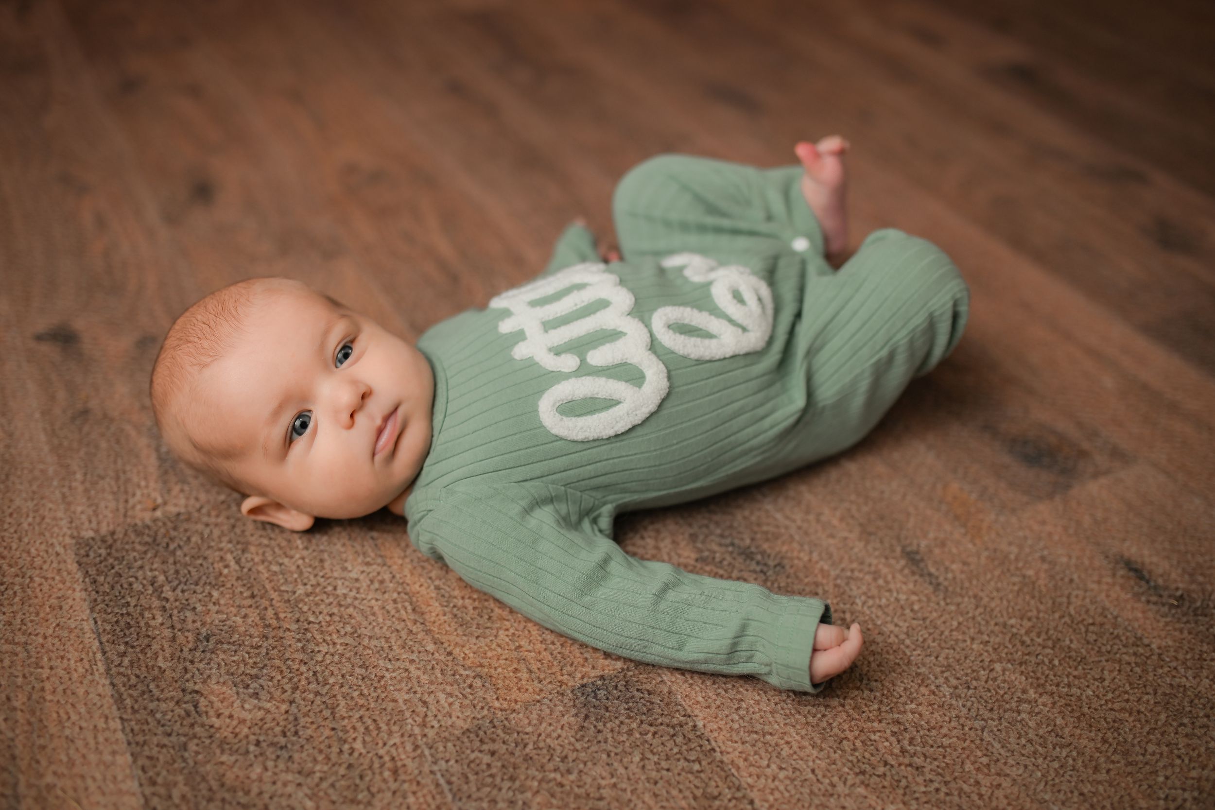 Infant wearing mint green outfit resting on brown carpet during portrait session.