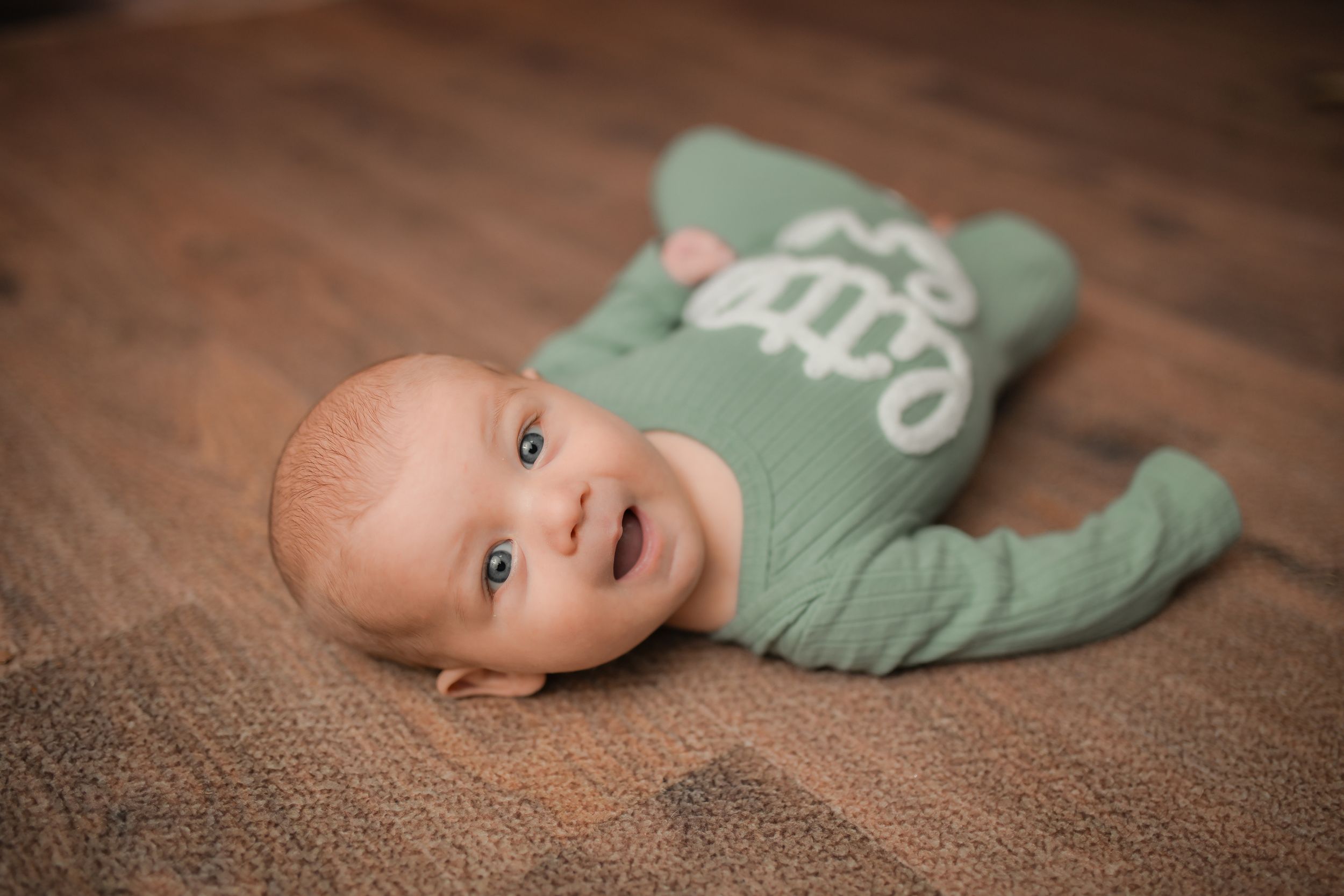 Infant smiling while wearing green outfit during professional photo session.