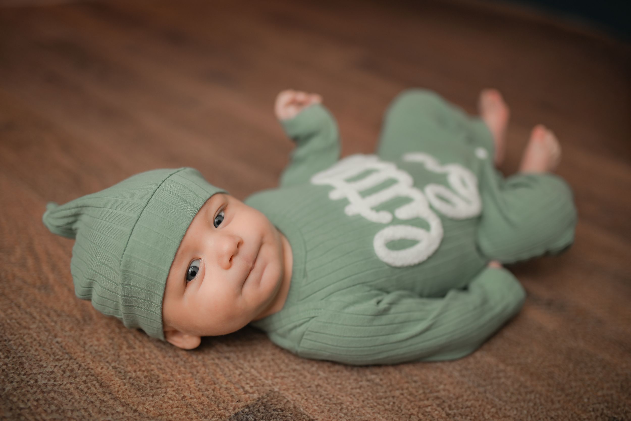 Infant in mint green sleeper during professional portrait session on brown surface.