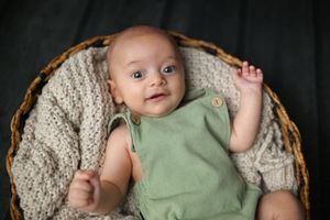 Baby wearing green romper resting in cozy knit-lined basket.
