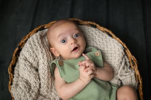 Infant in sage green outfit lying in woven basket with cream knit lining.
