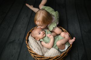 Two children posed together in round wicker basket with cream knit lining.