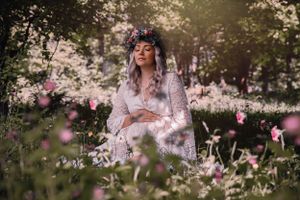 Ethereal figure in lace dress sits among wildflowers at sunset with bokeh effect in dreamy outdoor setting.