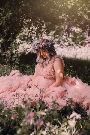 A dreamy outdoor portrait featuring a flowing pink tulle gown and floral crown amidst wildflowers in soft sunlight.