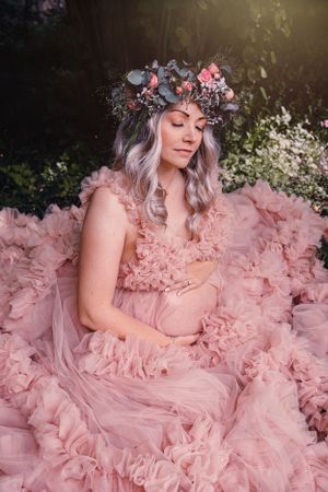 Ethereal maternity photo featuring a flowing pink ruffled gown and floral crown in a dreamy garden setting.