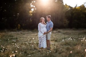 A couple stands together in a sunlit meadow with wildflowers during golden hour sunset.