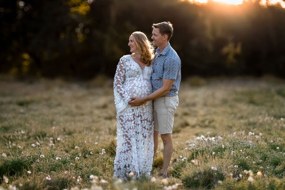 A couple embraces in a golden sunlit meadow at sunset while wearing light summer attire.