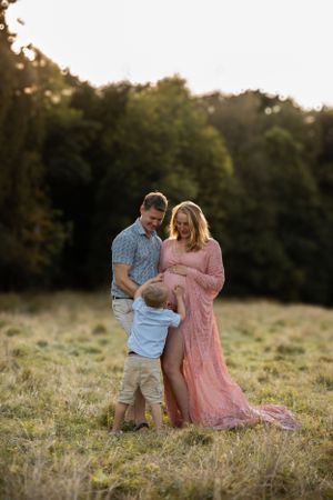 A family stands together in a sunlit meadow at golden hour, with trees in the background.