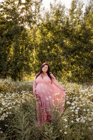 A flowing pink lace dress stands out against a field of white daisies and green trees at sunset.