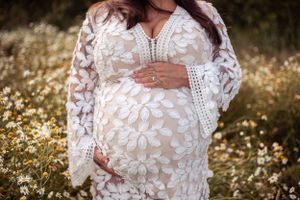 Elegant white lace maternity dress photographed in a wildflower field during golden hour.