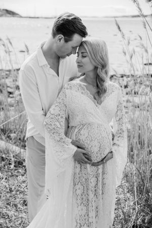 Intimate black and white maternity portrait of a couple embracing in a field of tall grass.