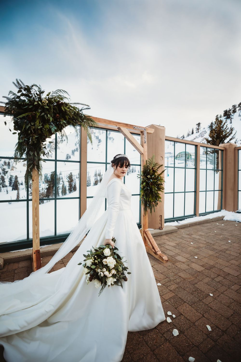 Bride in flowing wedding gown holding her bouquet with white flowers against a snowy mountain background in Utah