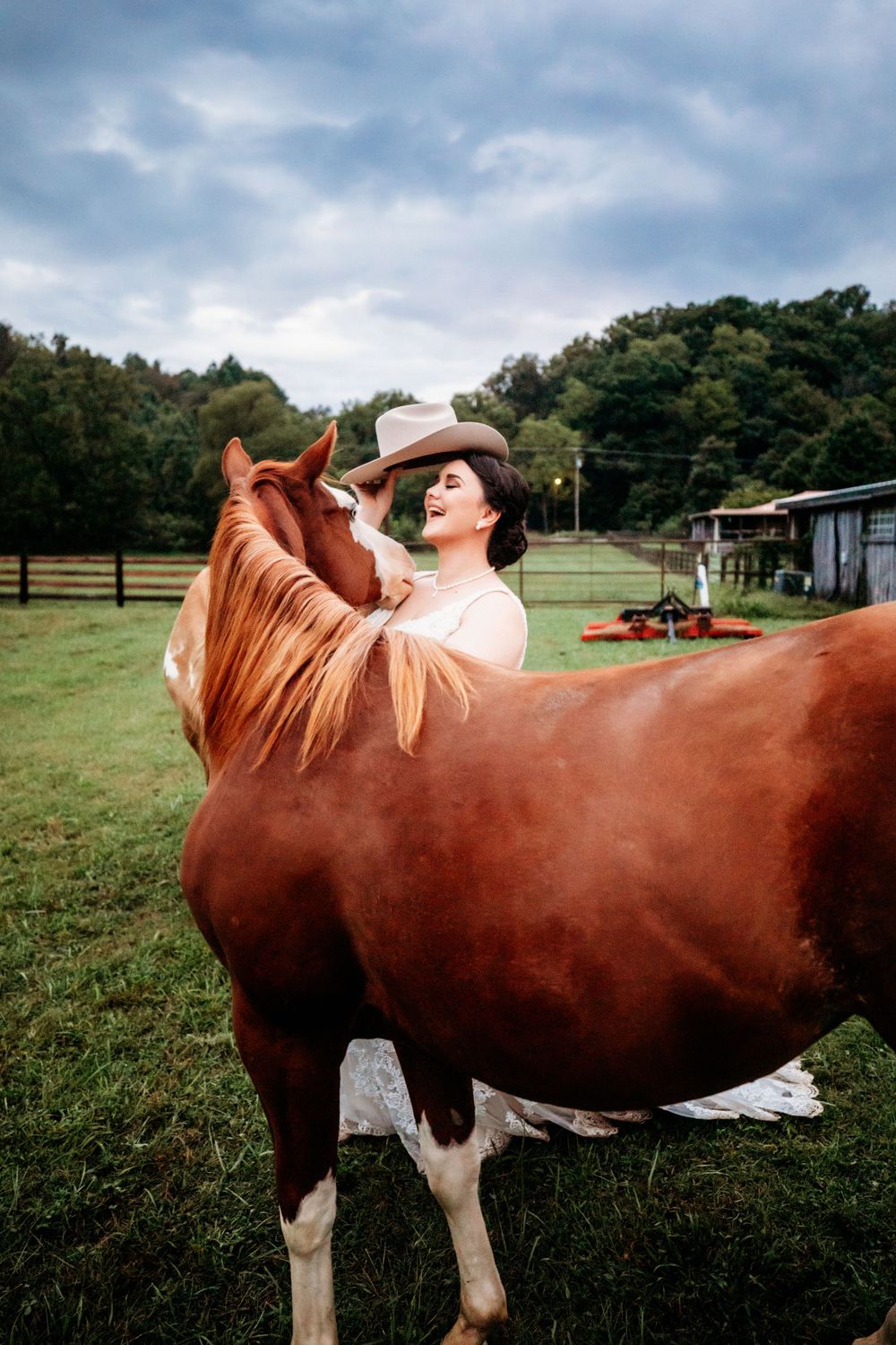 Bride lifting her hat while standing with horse in field at Cactus Creek in Dickson, TN