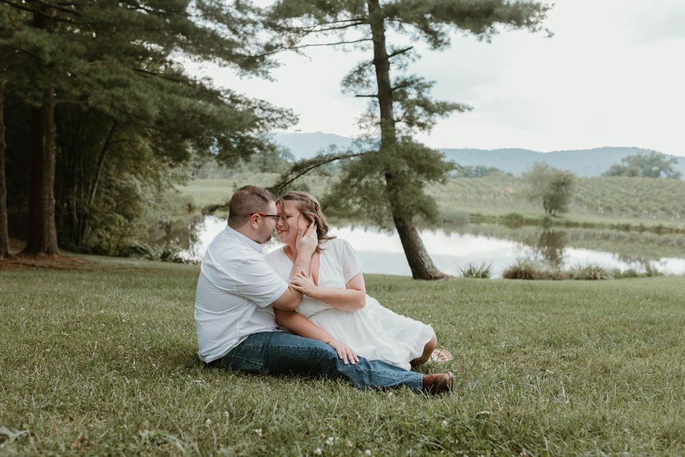 Romantic couple relaxing on grassy hillside near lake during sunset.