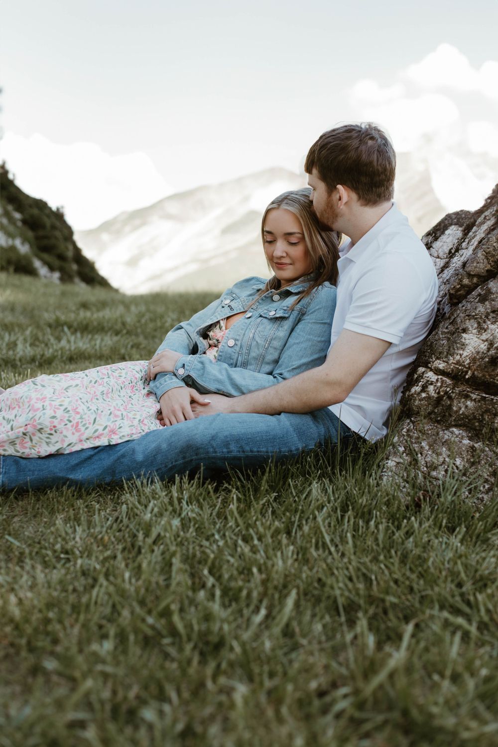 Couple relaxing together on a grassy hillside during a romantic mountain photoshoot.