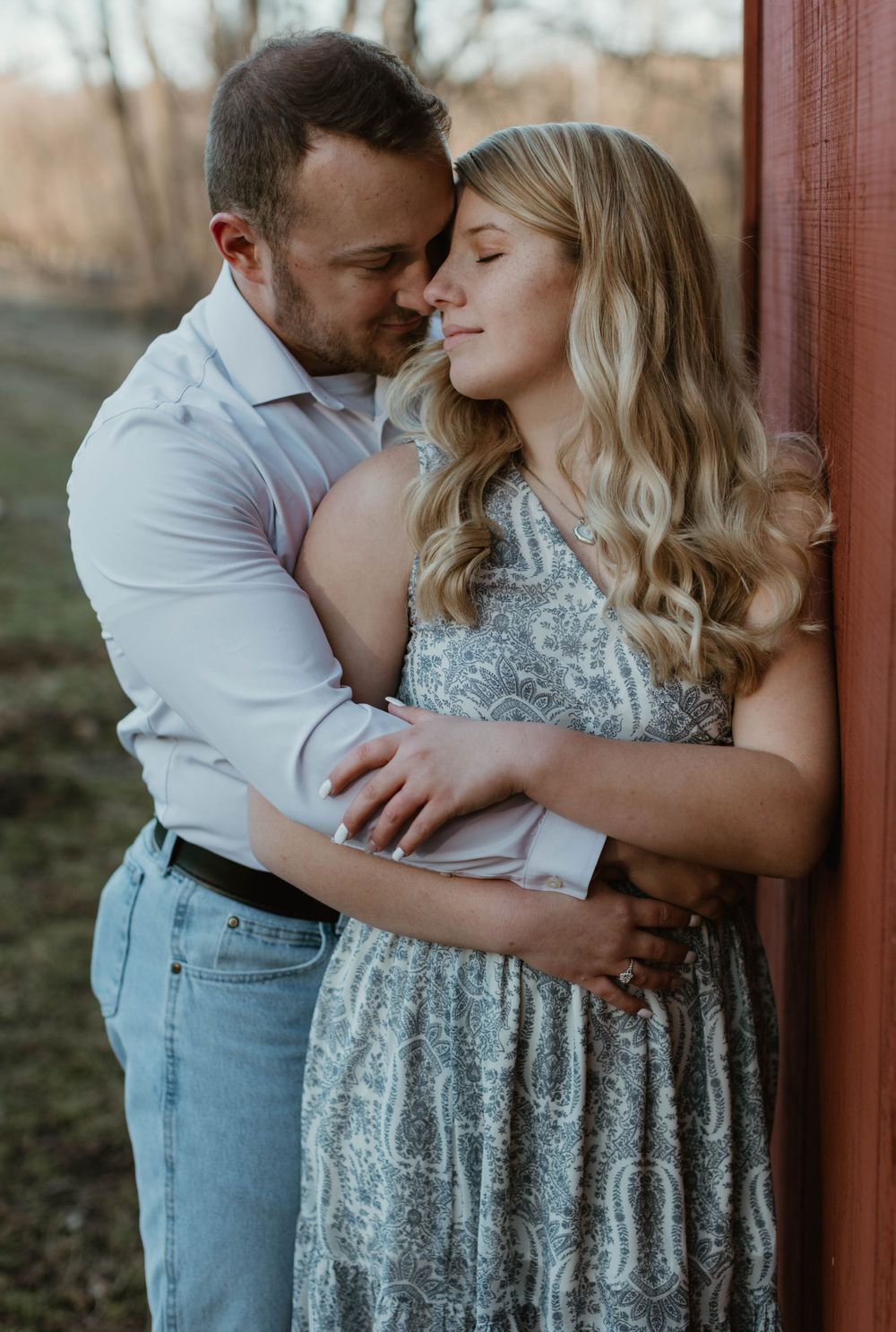 Romantic couple embracing in formal wear against a rustic red wall during sunset.