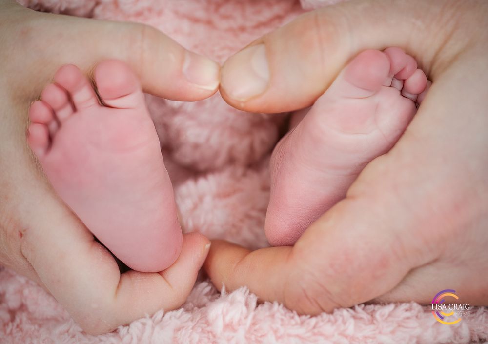 Tiny baby feet resting on soft pink fabric with gentle hands cradling them.