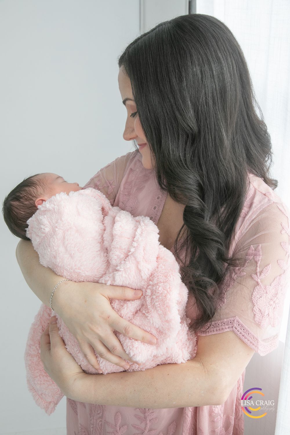 Four sequential images show a mother in pink attire lovingly cradling and bonding with a small baby in soft pink clothing.