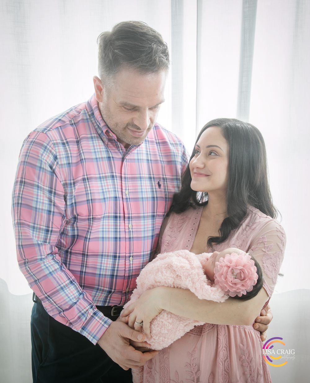 A couple shares tender moments in a bright interior space wearing pink and plaid clothing while embracing each other.