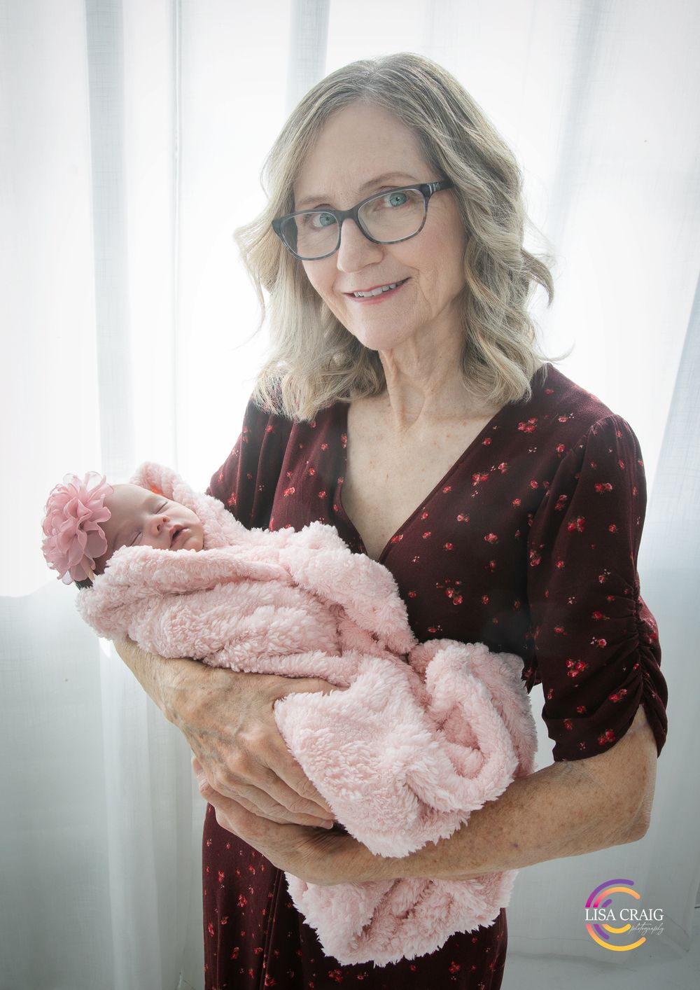 A person wearing glasses and a black polka dot top holds a soft pink plush blanket in a bright room.