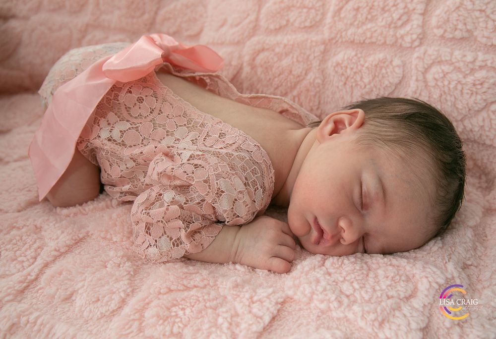 Sleeping baby lying on pink lace blanket in peaceful slumber during newborn photography session.